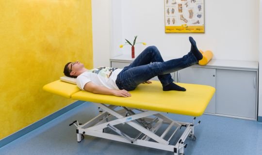 Patient auf gelber Therapieliege bei Physiotherapie-Übung im Behandlungsraum.