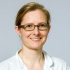 Porträt einer lächelnden Frau mit Brille in weißem Kittel.