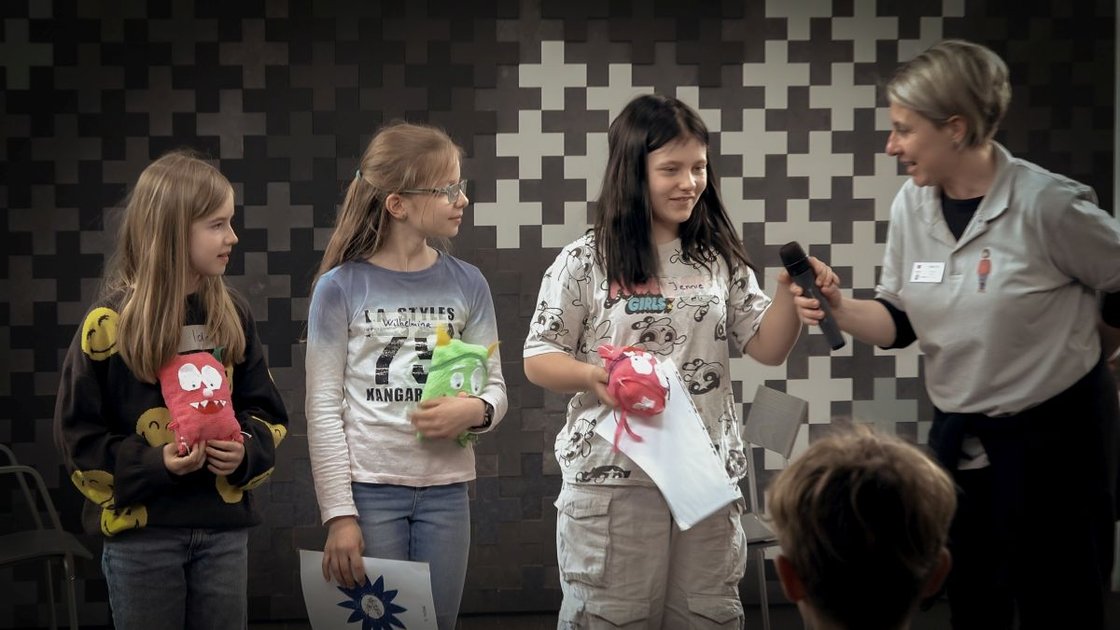 Drei Mädchen präsentieren Stoffpuppen bei einem Bildungsprojekt im Krankenhaus.