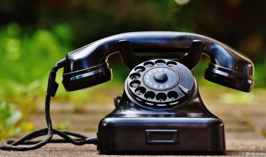 Schwarzes Wählscheibentelefon auf Holztisch im Freien.