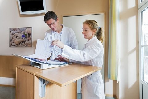Zwei Ärzte besprechen Unterlagen in einem hellen Krankenhausraum.