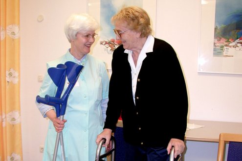 Grüne Dame hilft älterer Frau mit Gehhilfe im Krankenhaus.