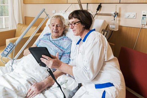 Pflegekraft zeigt älterem Patienten im Krankenhaus ein Tablet.