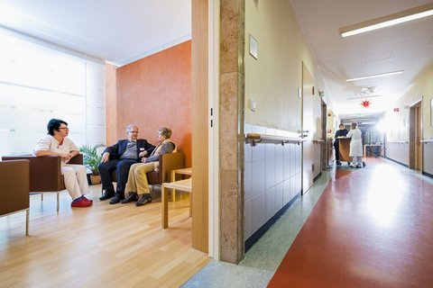 Pflegekraft im Gespräch mit zwei älteren Personen im Wartebereich der Palliativstation.