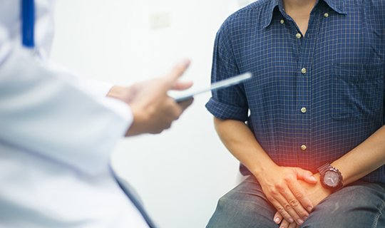 Mann beim Arztgespräch, hält schmerzenden Unterleib, symbolisiert urologisches Problem.