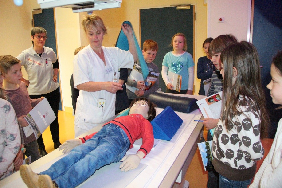 Kinder betrachten Puppe bei Krankenhausprojekt Jonas will's wissen.