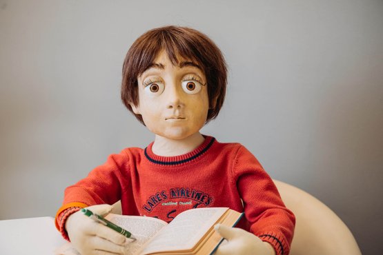 Puppe Jonas im roten Pullover liest konzentriert in einem Buch.