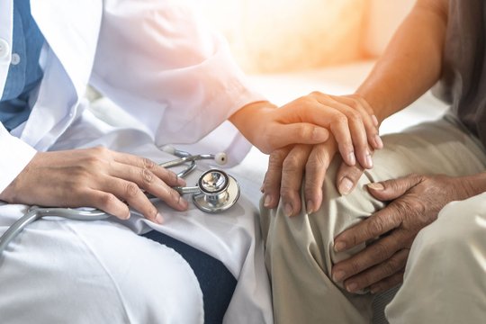 Arzt hält Hand eines älteren Patienten, symbolisiert Betreuung in der Geriatrie.