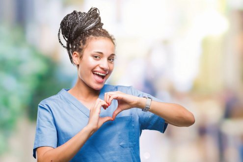 Pflegekraft in blauer Uniform formt Herz mit Händen, lächelt freundlich.