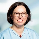 Porträt einer lächelnden Frau mit Brille in blauer Kleidung.