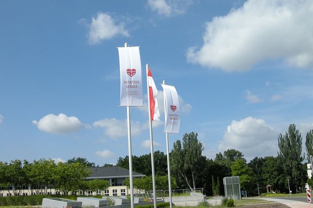 Drei Fahnen mit Martha-Maria-Logo wehen vor blauem Himmel über Querfurt.