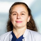 Porträt einer lächelnden Ärztin in weißem Kittel vor unscharfem Hintergrund.