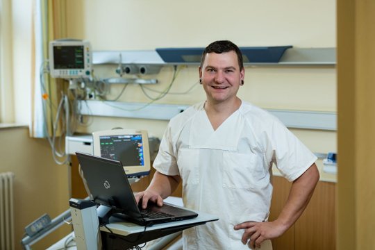 Krankenpfleger in weißem Kittel arbeitet mit Laptop in Krankenhausumgebung.