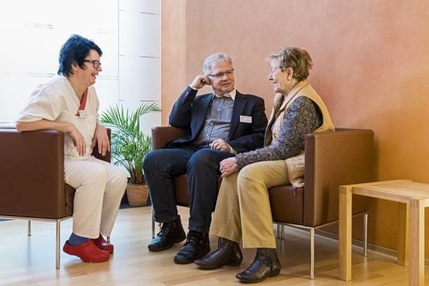 Pflegekraft im Gespräch mit zwei älteren Personen im Wartebereich der Palliativstation.