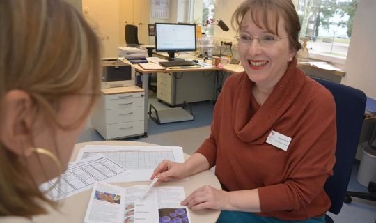 Krankenhausmitarbeiterin erklärt einer Patientin Informationen in einem Büro.