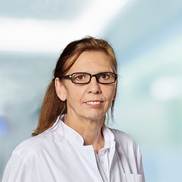 Porträt einer Frau in Arztkittel vor einem unscharfen Hintergrund.