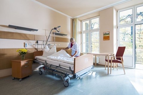 Pflegekraft richtet Bett in hellem Einzelzimmer der Palliativstation.