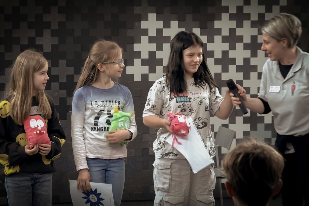 Drei Mädchen präsentieren Stoffpuppen bei einem Bildungsprojekt im Krankenhaus.