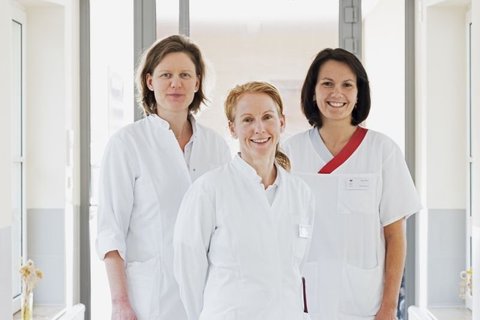 Drei Pflegekräfte in weißen Arbeitsuniformen auf der Palliativstation.