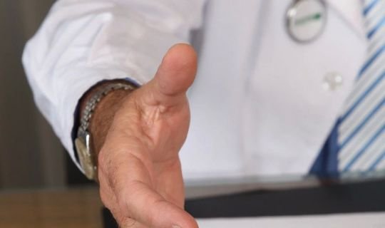 Arzt streckt Hand zum Händedruck aus, symbolisiert Begrüßung und Vertrauen.
