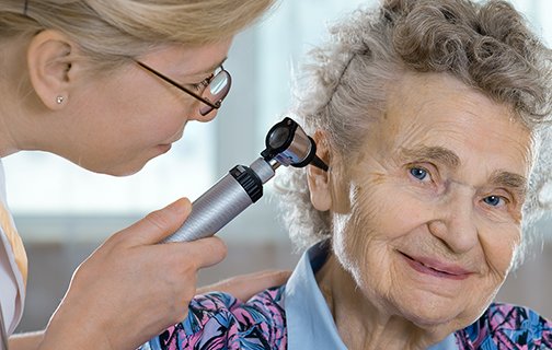 Ärztin untersucht Ohr einer älteren Patientin mit Otoskop.