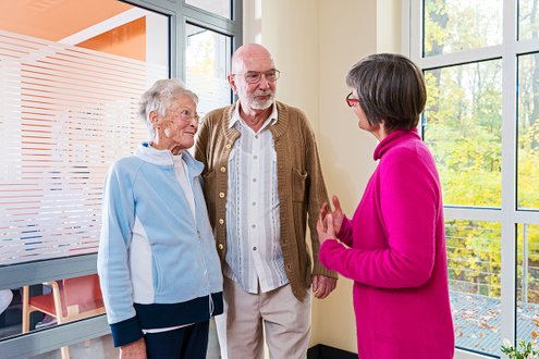 Gespräch zwischen Seelsorgerin und älterem Paar im Krankenhausflur.