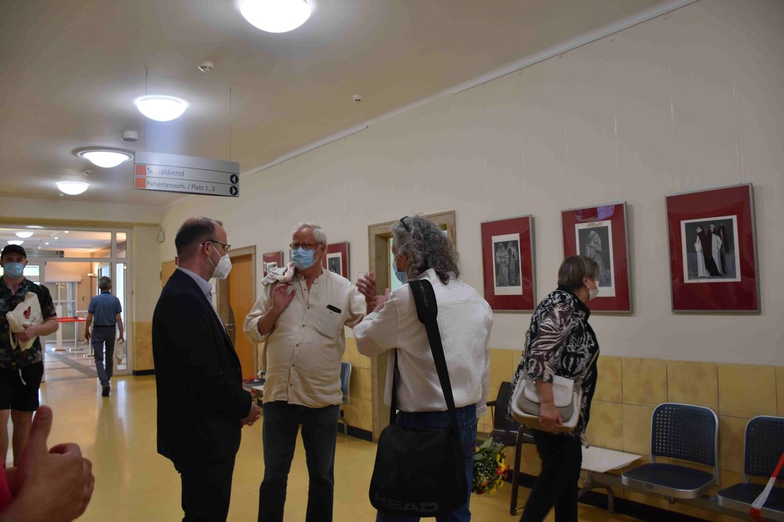 Menschen mit Masken unterhalten sich im Krankenhausflur vor Kunstwerken.