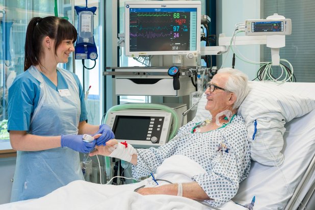 Pflegekraft betreut lächelnden Patienten im Krankenhausbett mit medizinischen Monitoren.