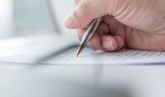 Nahaufnahme einer Hand, die ein Formular mit Kugelschreiber ausfüllt.