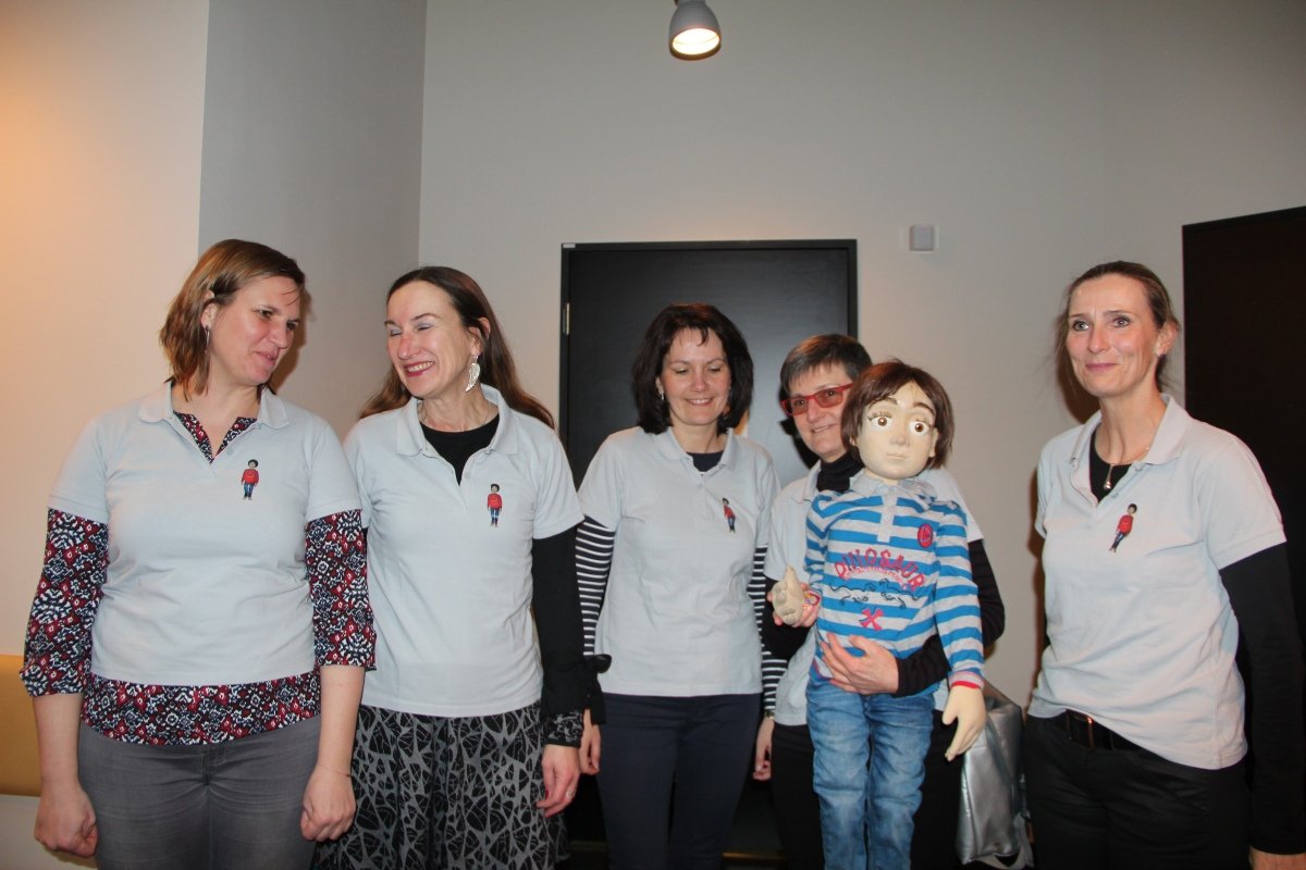 Fünf Frauen in weißen T-Shirts mit Puppe Jonas während eines Krankenhausprojekts.