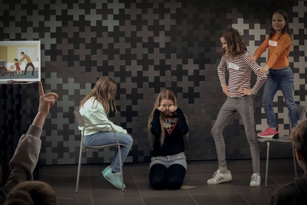 Kinder stellen eine Szene im Krankenhaus dar, Publikum schaut zu.