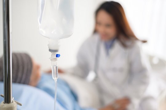 Nahaufnahme einer Infusion im Krankenhaus, Patient im Hintergrund unscharf.