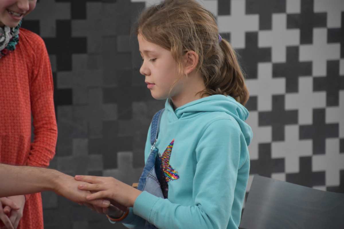 Mädchen in blauem Hoodie hält sanft eine Hand, konzentriert.