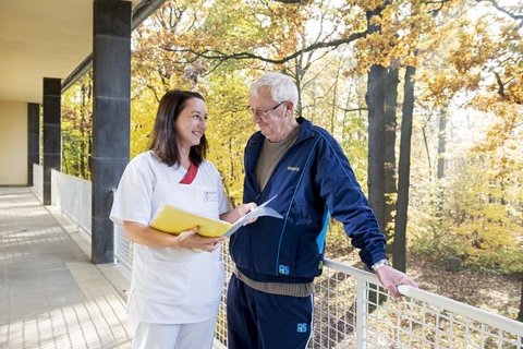 Pflegekraft im Gespräch mit älterem Mann auf Palliativstation im Herbst.