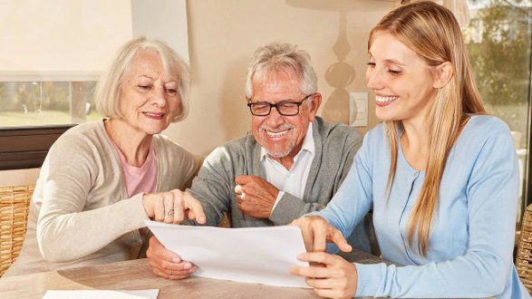 Ältere Frau, älterer Mann und junge Frau lächeln und betrachten ein Dokument.