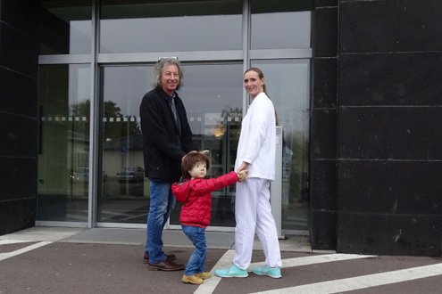 Person mit Kind und Puppe vor Krankenhaus Martha-Maria Dölau.