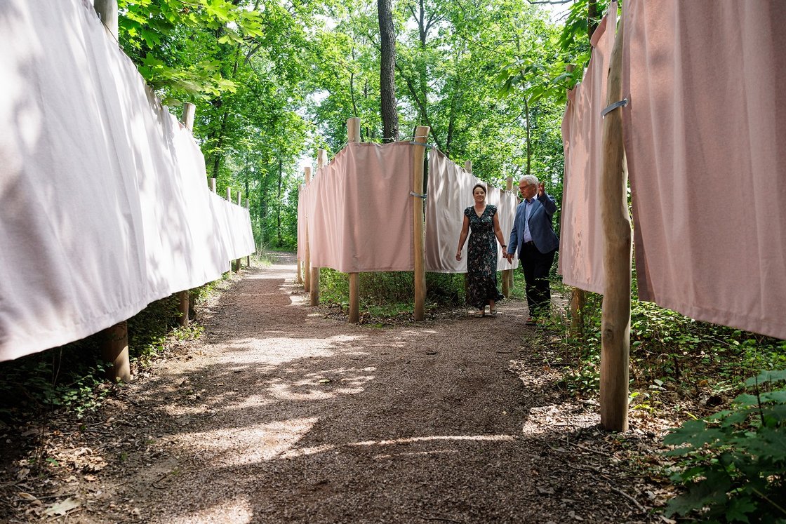 Zwei Menschen spazieren durch einen Waldweg mit Stoffbahnen im Krankenhausgarten.