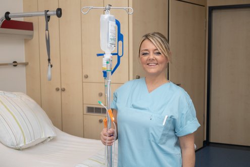 Krankenschwester im Krankenhauszimmer mit Infusionsständer und Lächeln.