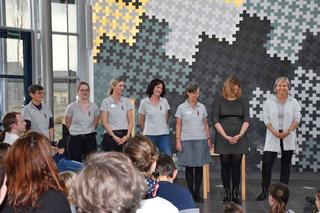 Gruppe von medizinischen Fachkräften steht lächelnd vor Publikum im Krankenhaus.