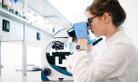 Wissenschaftlerin im Labor benutzt ein Mikroskop zur Untersuchung.