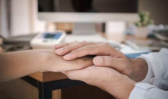 Arzt hält Hand eines Patienten als Zeichen von Unterstützung und Vertrauen.