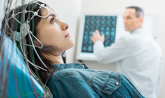 Patientin mit EEG-Haube, Arzt analysiert Gehirnscans im Hintergrund.